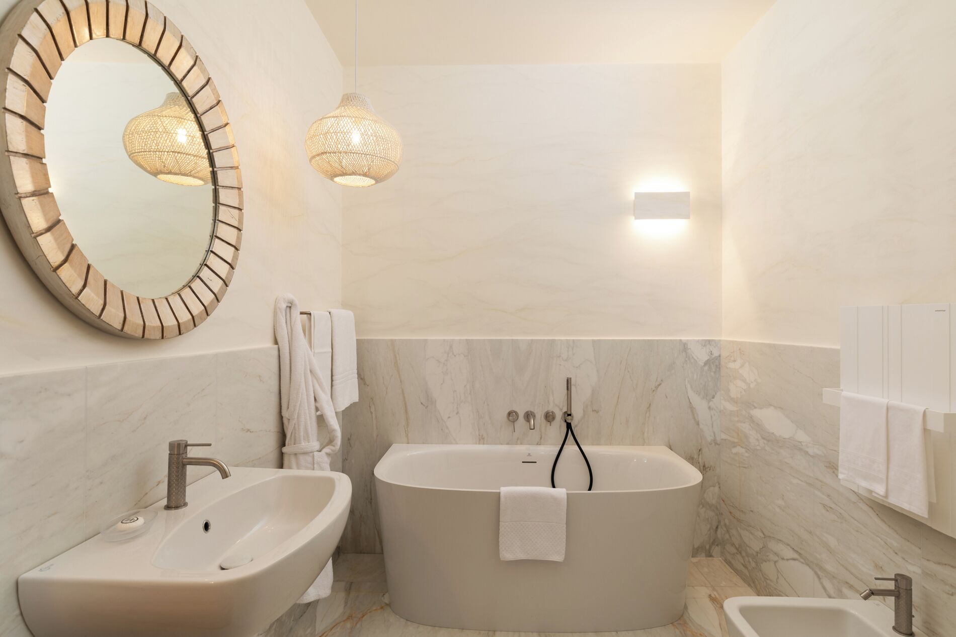 A modern bathroom with a freestanding bathtub, a pedestal sink, and a large mirror.