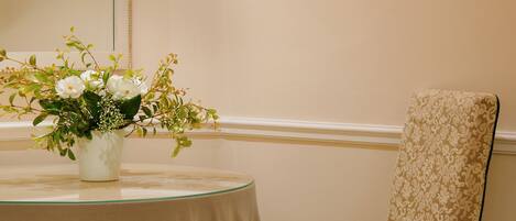 Ein Zimmer mit einem runden Tisch, einem Stuhl, einer Vase mit Blumen und Wandleuchten.