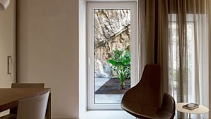Un salon moderne comprenant un coin repas, une grande fenêtre donnant sur un paysage rocheux, un fauteuil en cuir marron et une petite table d’appoint avec un livre.