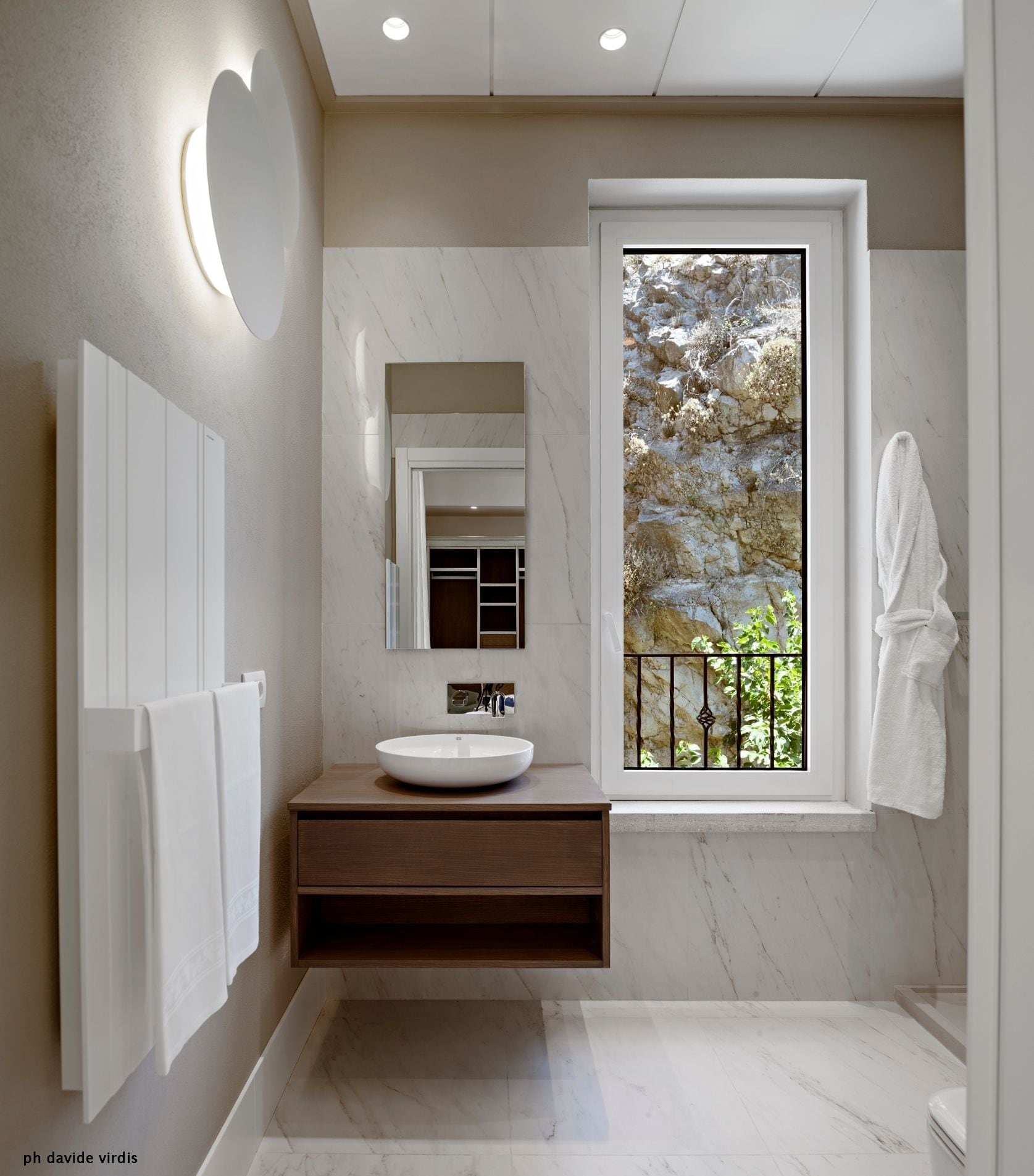 Un baño moderno con un lavamanos grande blanco, un tocador de madera, un espejo y una ventana con vistas a vegetación.