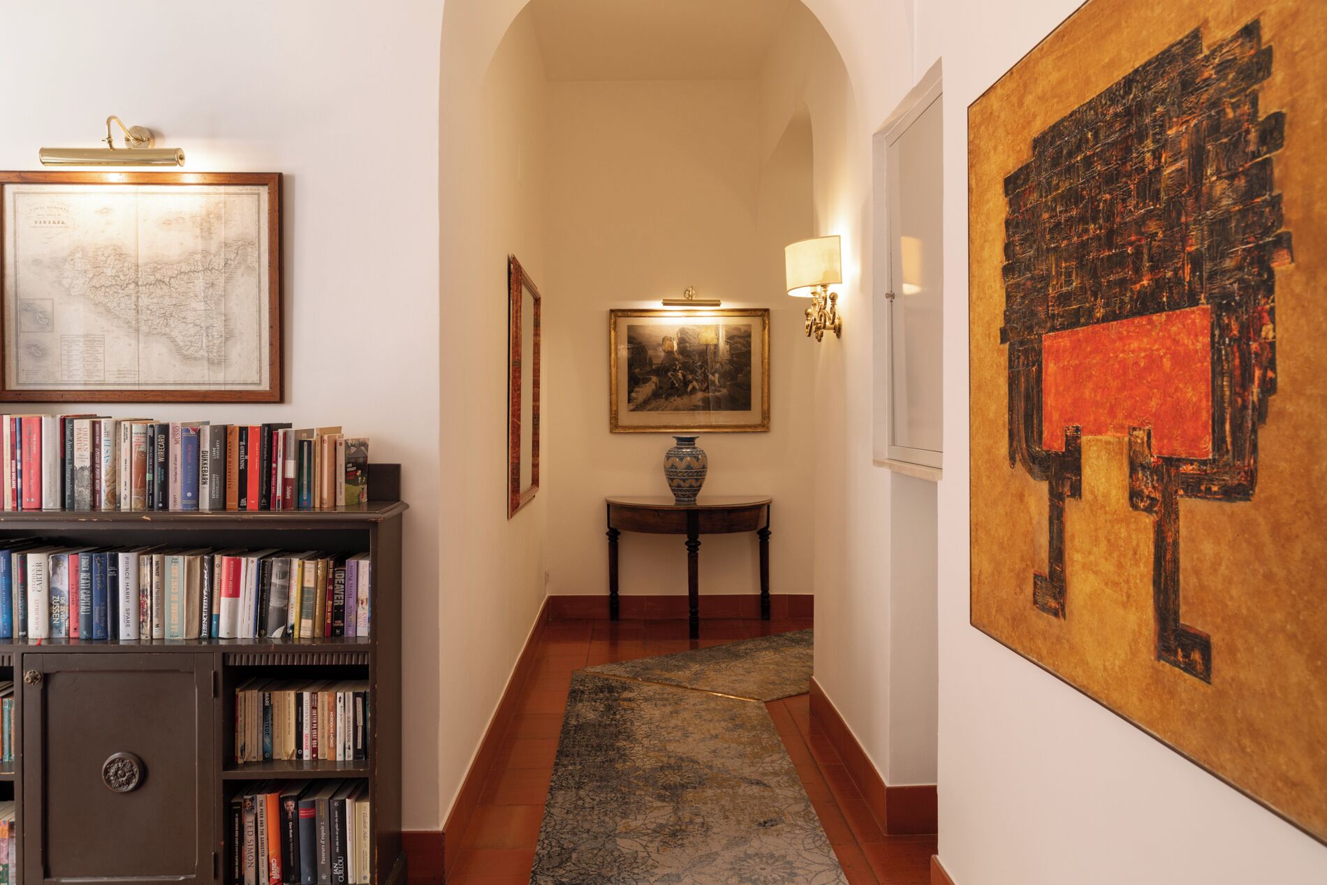 Un couloir avec une bibliothèque, une carte encadrée et une grande peinture abstraite.