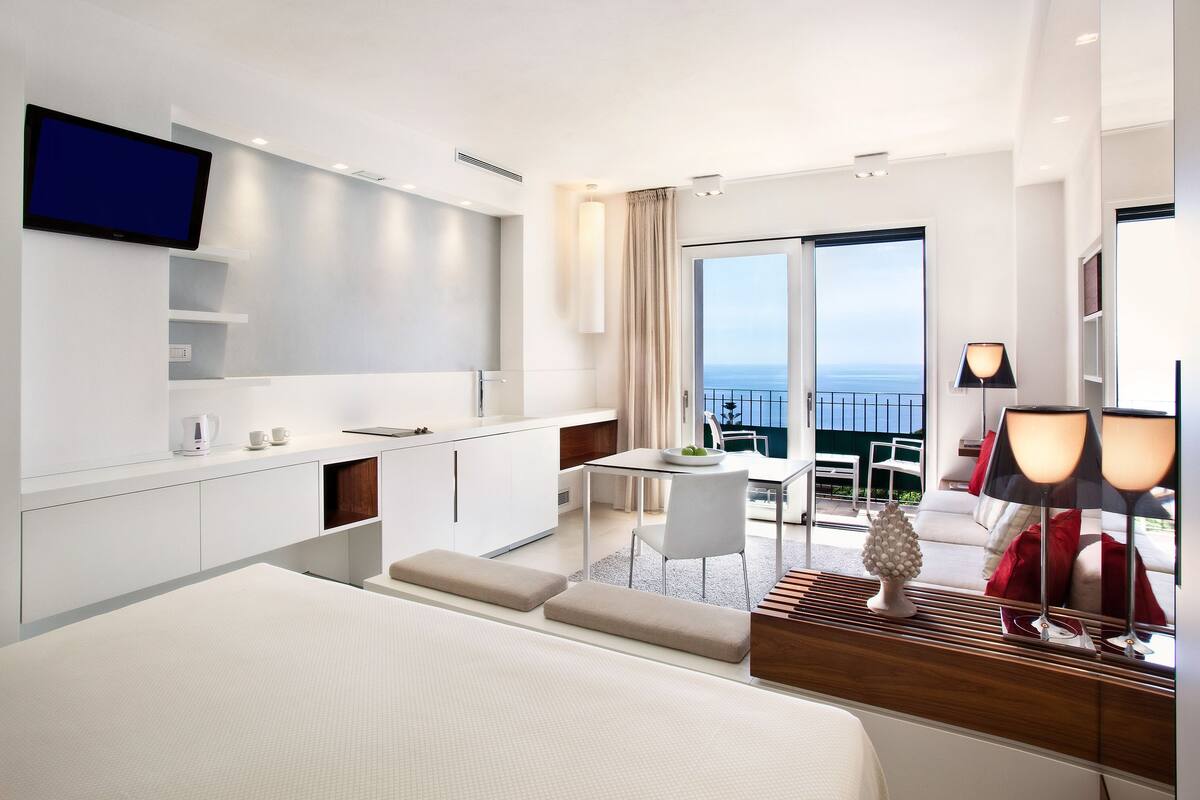 Een moderne hotelkamer met een groot bed, een kitchenette, een eethoek en een balkon met uitzicht.