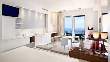 Una habitación de hotel moderna con una cama grande, kitchenette, zona de comedor y balcón con vistas.