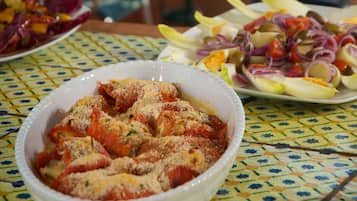 A poolside dining area with a table set for two, featuring a bowl of stuffed peppers and a plate of salad.