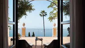 Un balcon avec des fauteuils en osier, une petite table et une vue sur la mer.