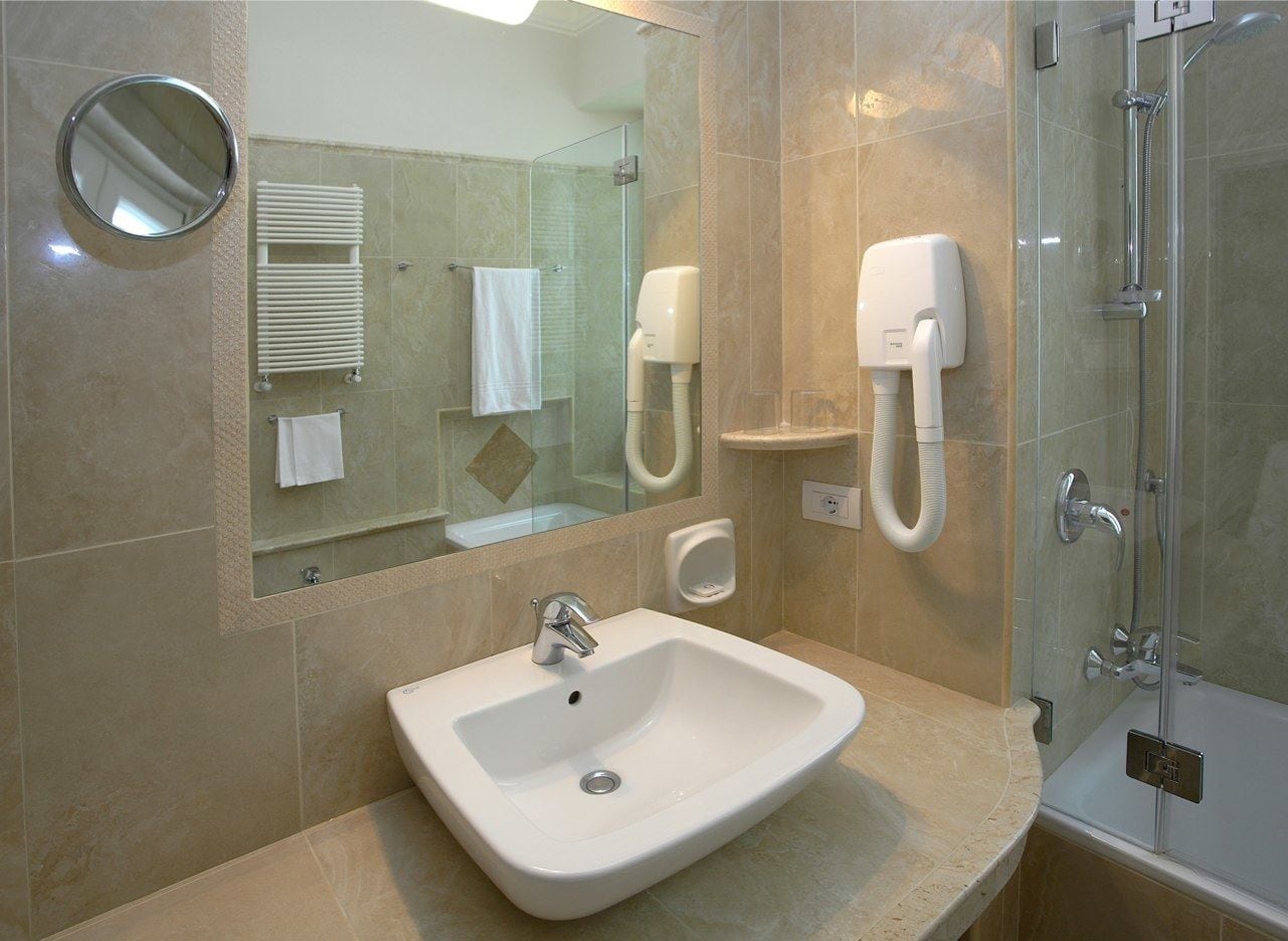 A bathroom with a sink, mirror, towel rack, and a glass-enclosed shower.