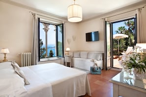 Quarto de hotel com cama, área de estar, televisão e vista para o exterior.