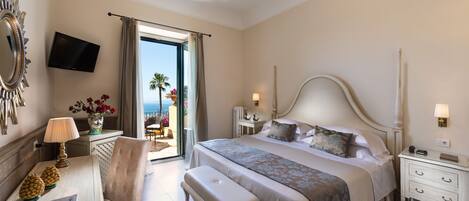 A bedroom with a large bed, bedside tables, a desk, a chair, and a TV on the wall.