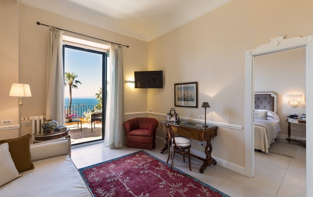 Ein Hotelzimmer mit Bett, Schreibtisch, Stuhl, Fernseher, einem Bild an der Wand und Blick auf den Ozean.
