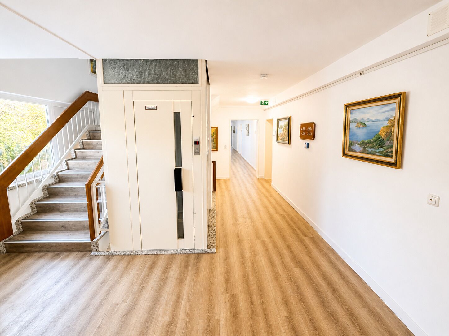 A hallway with a wooden staircase, a door with a sign, and framed artwork on the walls.