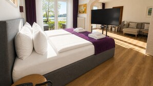 A hotel room with a large bed, a TV, a sofa, and a view of a lake. - Seehotel Schwanenhof (Moelln)