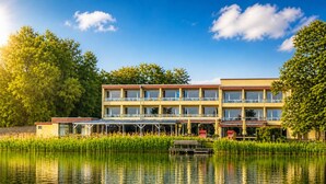 A multi-story hotel with a pool in front, surrounded by greenery. - Seehotel Schwanenhof (Moelln)