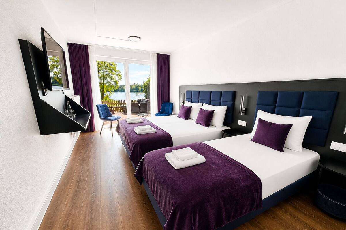 Quarto de hotel com duas camas, televisão, área de estar com cadeiras e vista para o exterior.