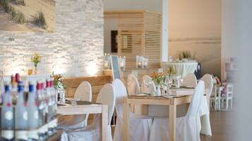 Een restaurant met witte stoelen, houten tafels en een stenen muur.