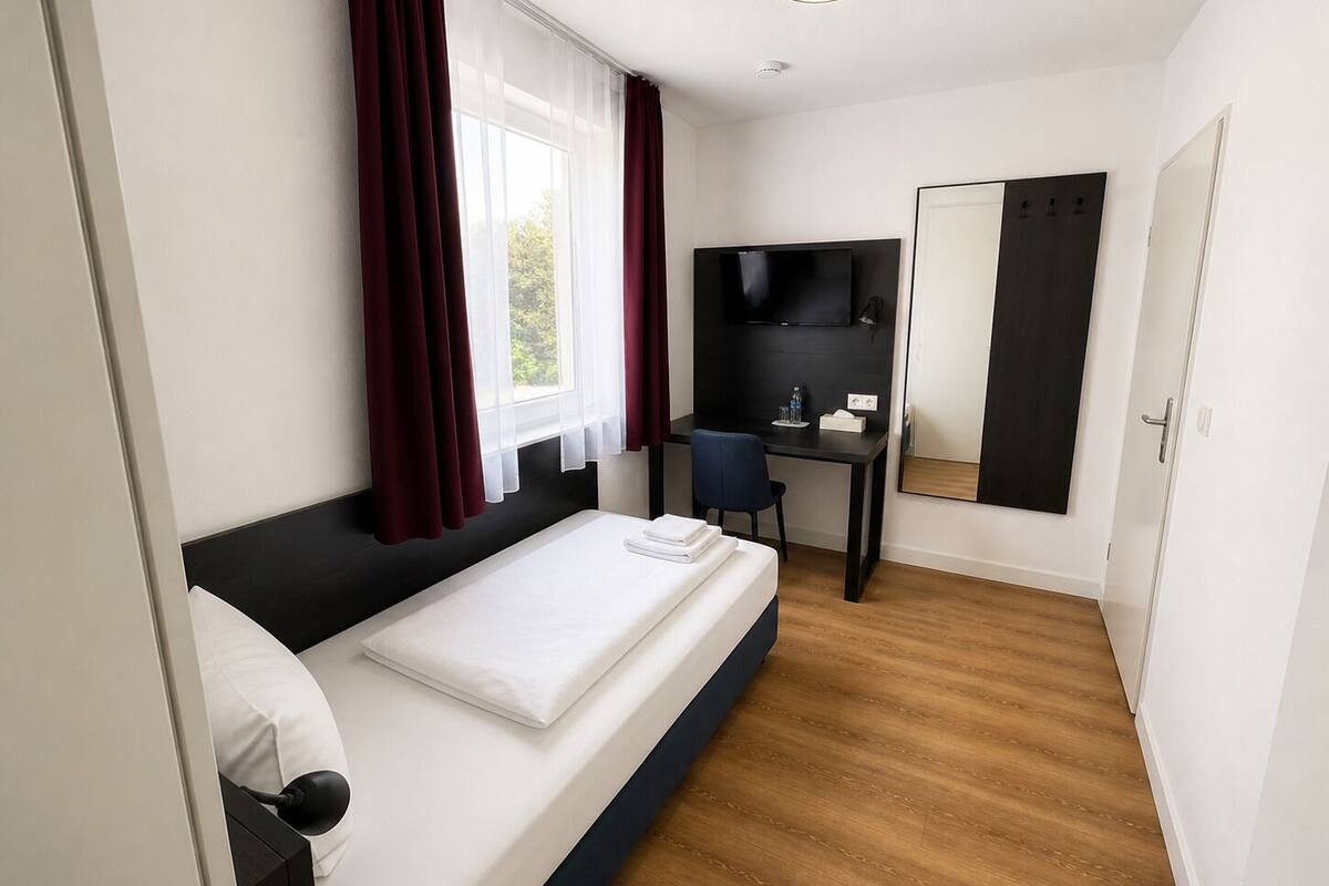 Quarto com cama, escrivaninha, cadeira, televisão e espelho.