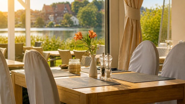 A table set for dining with a view of a lake and buildings in the background. - Seehotel Schwanenhof (Moelln)