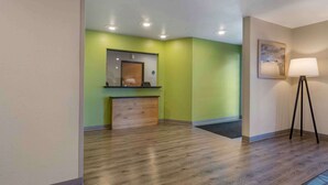 Un espace d’accueil avec un mur végétal, un plancher en bois, un bureau avec un ordinateur, un miroir et un lampadaire.