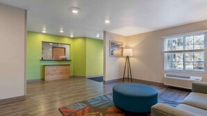 Une chambre d’hôtel avec un plancher en bois, un pouf bleu, une lampe sur pied et une fenêtre avec des stores.