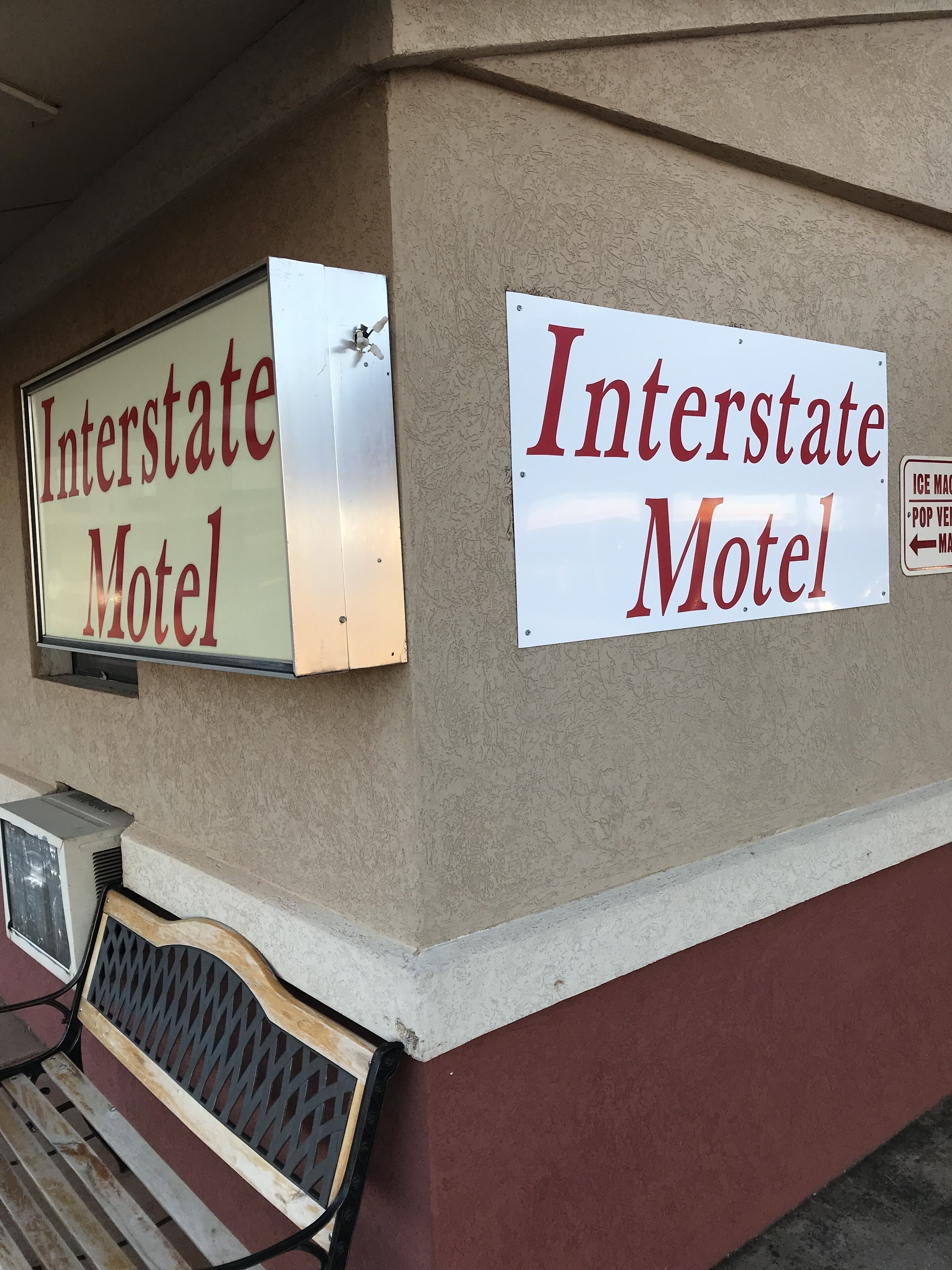 A motel sign with "Interstate Motel" written in red on a white background, mounted on a beige wall.