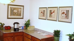 Una cocina con armarios de madera, encimera de granito, cafetera y cuadros con motivos florales en la pared.