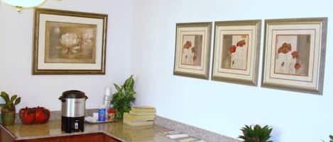 A kitchen with wooden cabinets, a granite countertop, a coffee maker, and framed floral artwork on the wall.