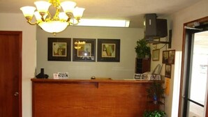 Una recepción con mostrador de madera, una araña, cuadros en la pared y una planta en maceta.