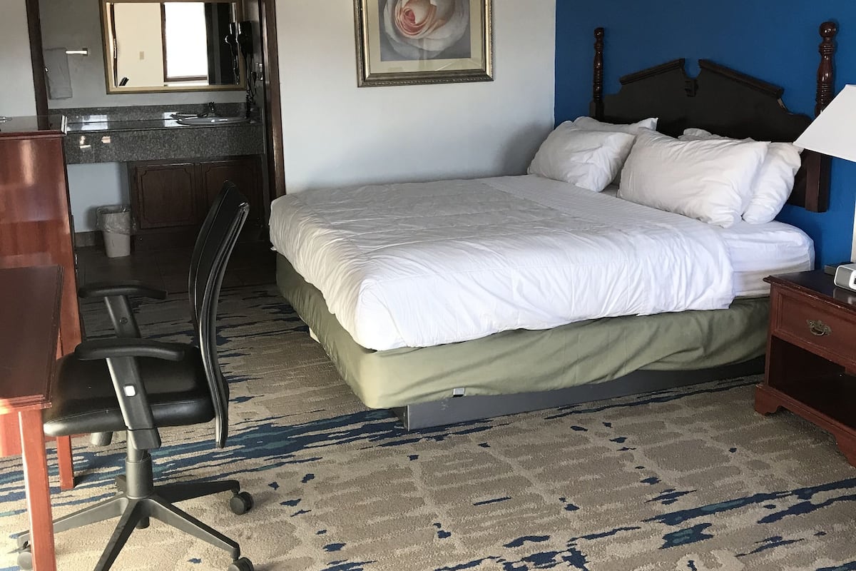 A hotel room with a bed, a desk, a chair, and a painting on the wall.