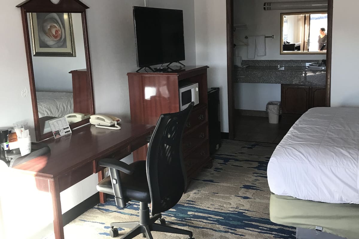 A hotel room with a bed, a desk with a chair, a television, a mirror, and a microwave.