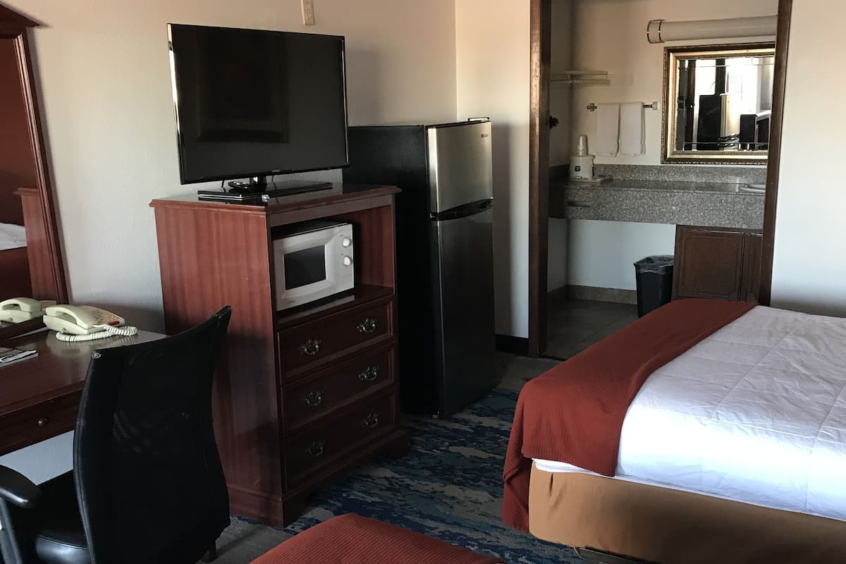 A hotel room with a bed, a desk with a telephone, a microwave, a refrigerator, and a television.