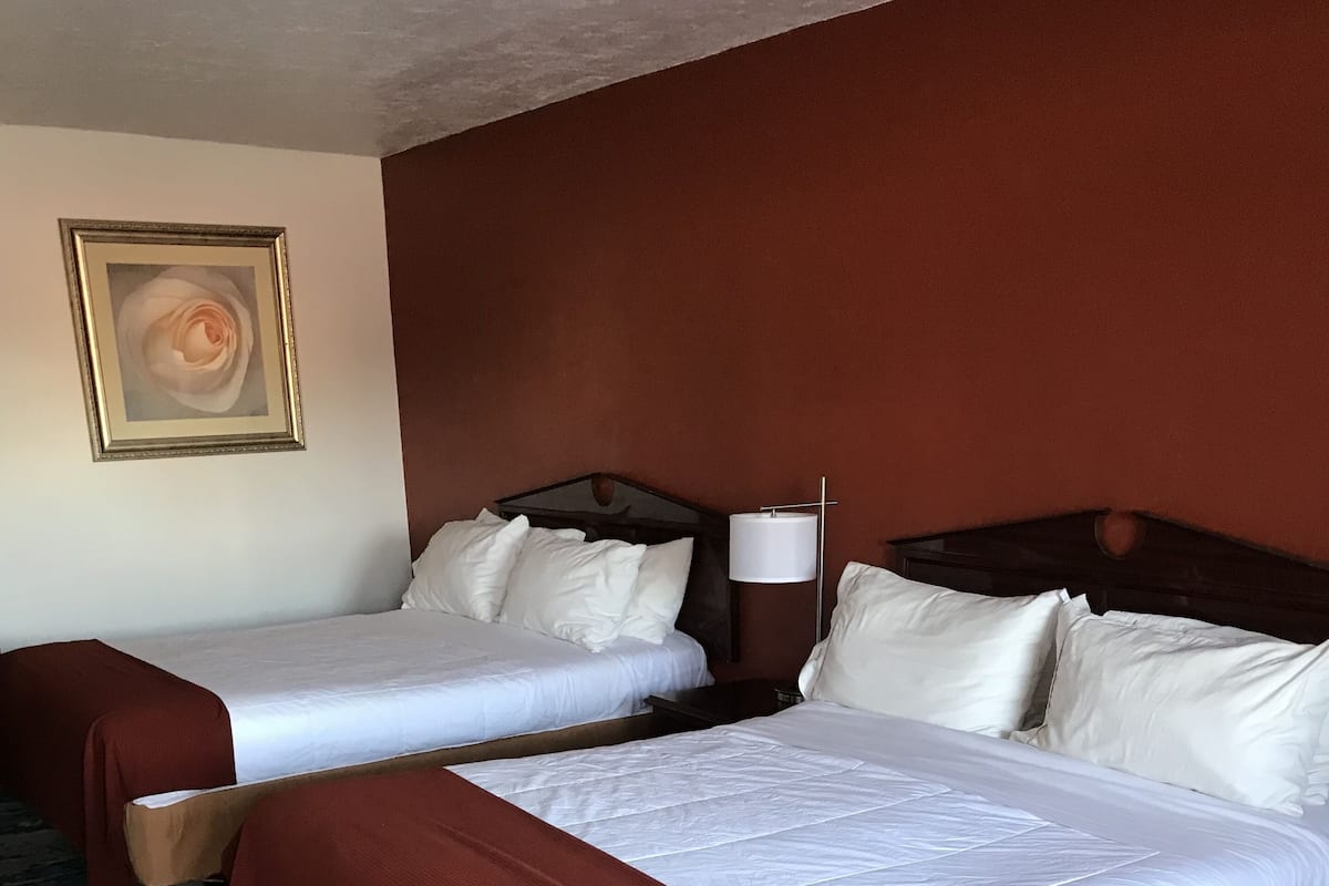 A hotel room with two beds, a large window, and a carpeted floor.