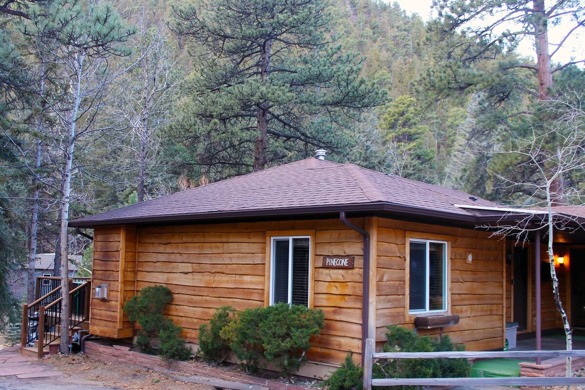 Une cabane en bois avec un toit en pente, une cheminée et une enseigne sur laquelle on peut lire « Pinecone ».