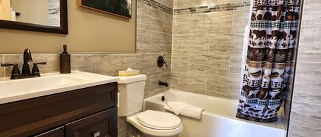 Ein Badezimmer mit Toilette, Badewanne, einer Duschvorhang mit Tiermotiven, einem Waschbecken mit dunklem Wasserhahn und einem gerahmten Bild an der Wand.