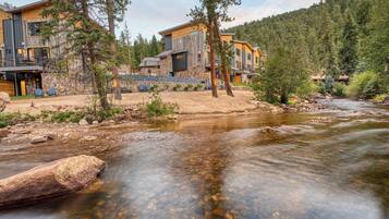 A riverside lodge with multiple buildings, a clear stream, and surrounding forest.