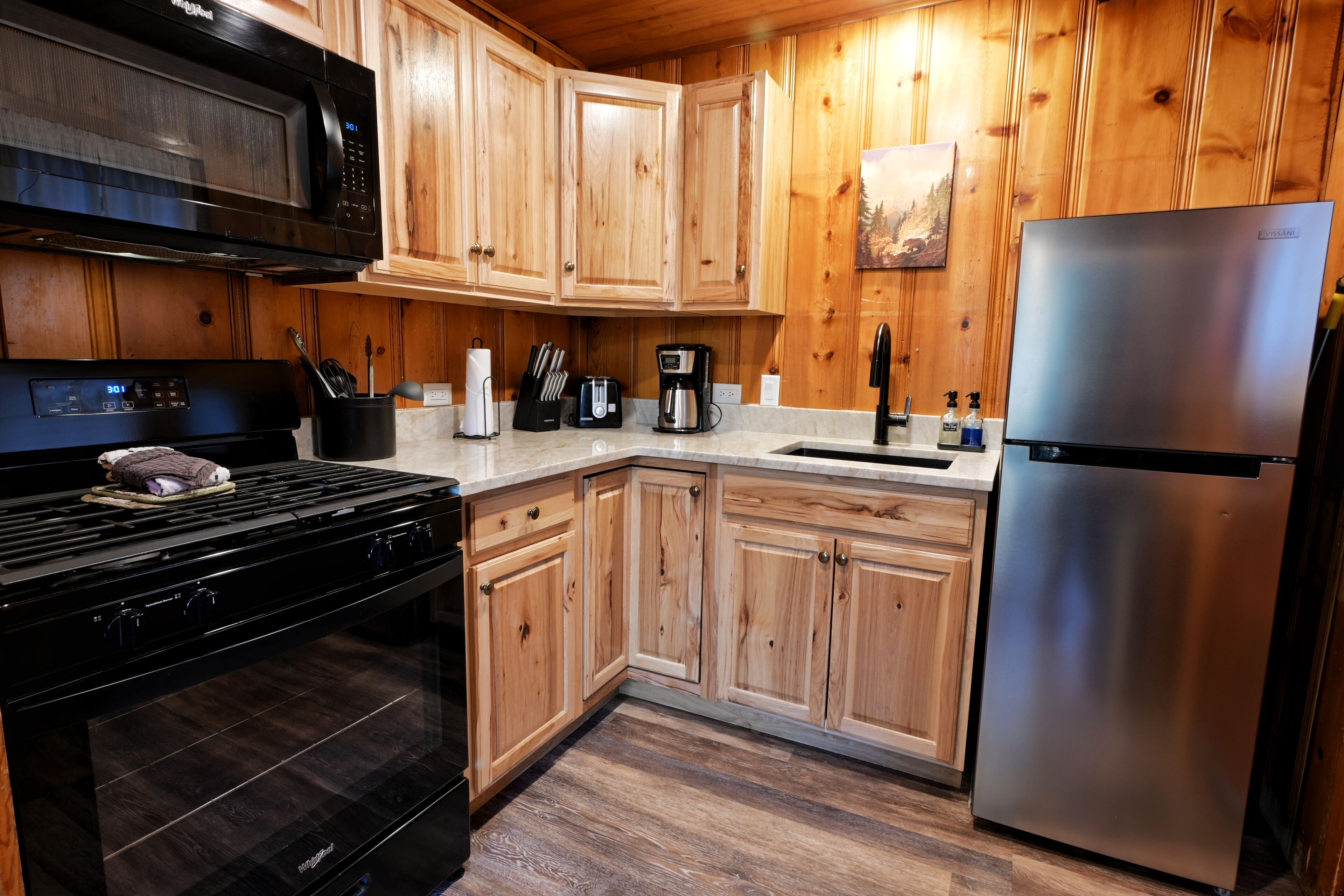 Una cocina con armarios de madera, un refrigerador de acero inoxidable, un microondas, una estufa y una cafetera.