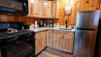 Una cocina con armarios de madera, un refrigerador de acero inoxidable, un microondas, una estufa y una cafetera.