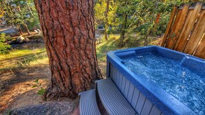 Un jacuzzi junto a una terraza de madera, rodeado de árboles y un entorno natural.