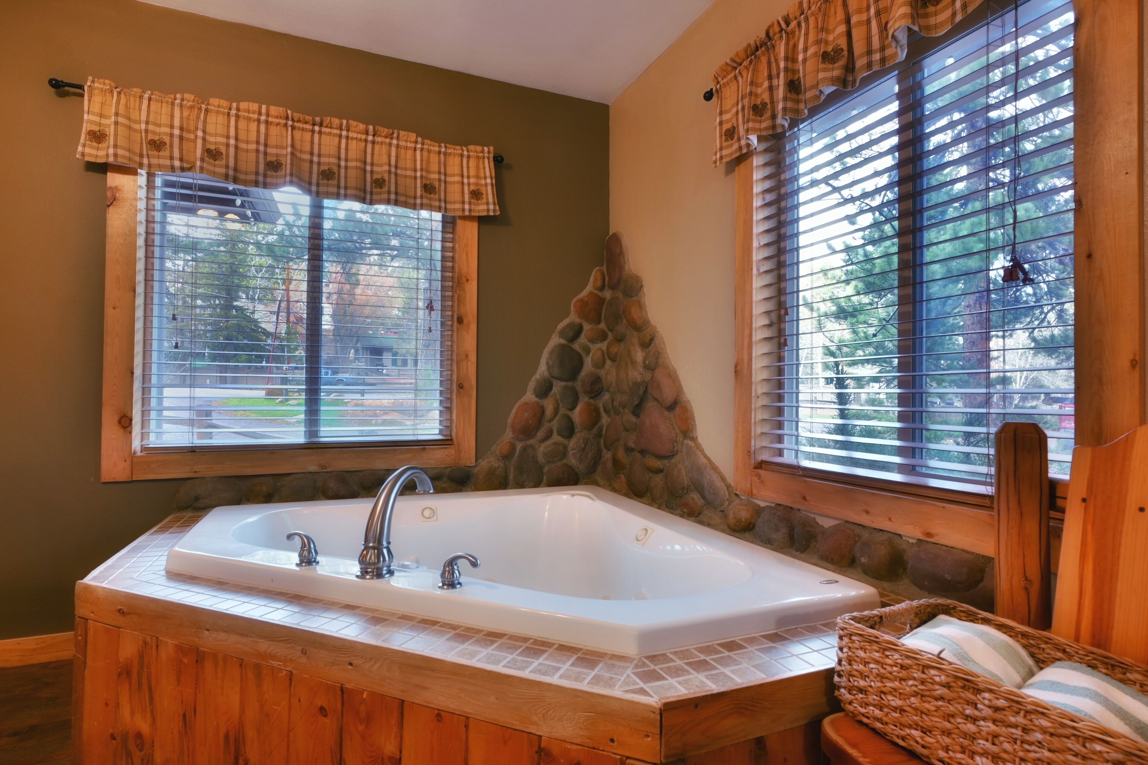 Un baño con una bañera grande, paredes de madera, detalles de piedra y ventanas con persianas.