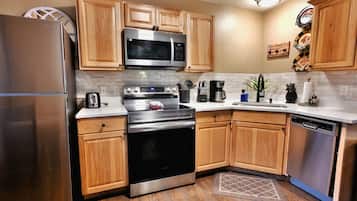A modern kitchen with stainless steel appliances, wooden cabinets, and a white countertop.