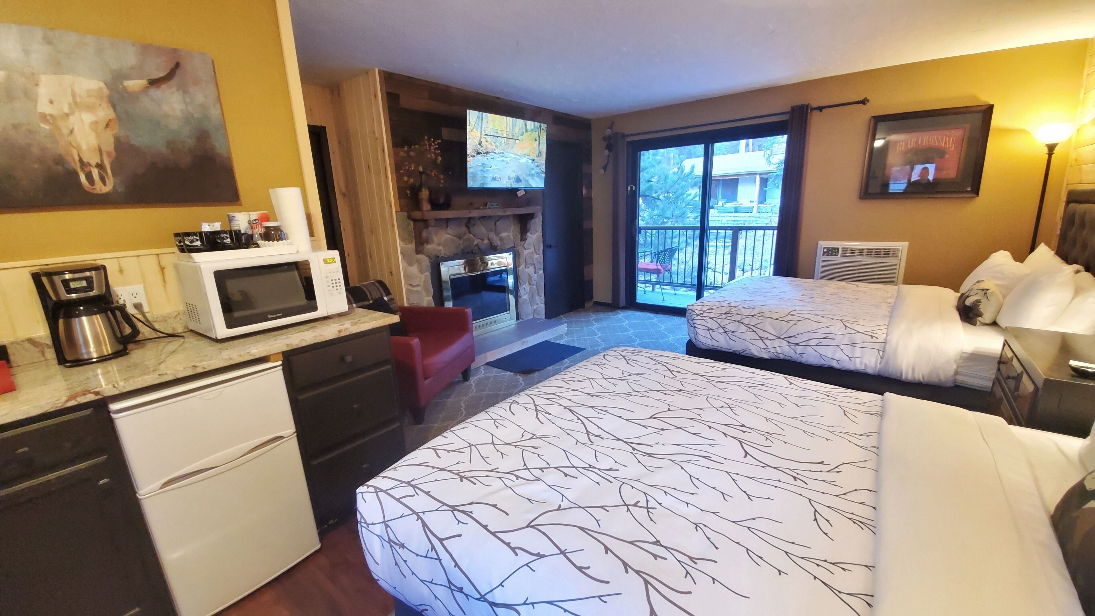A hotel room with two beds, a kitchenette, a fireplace, and a TV.
