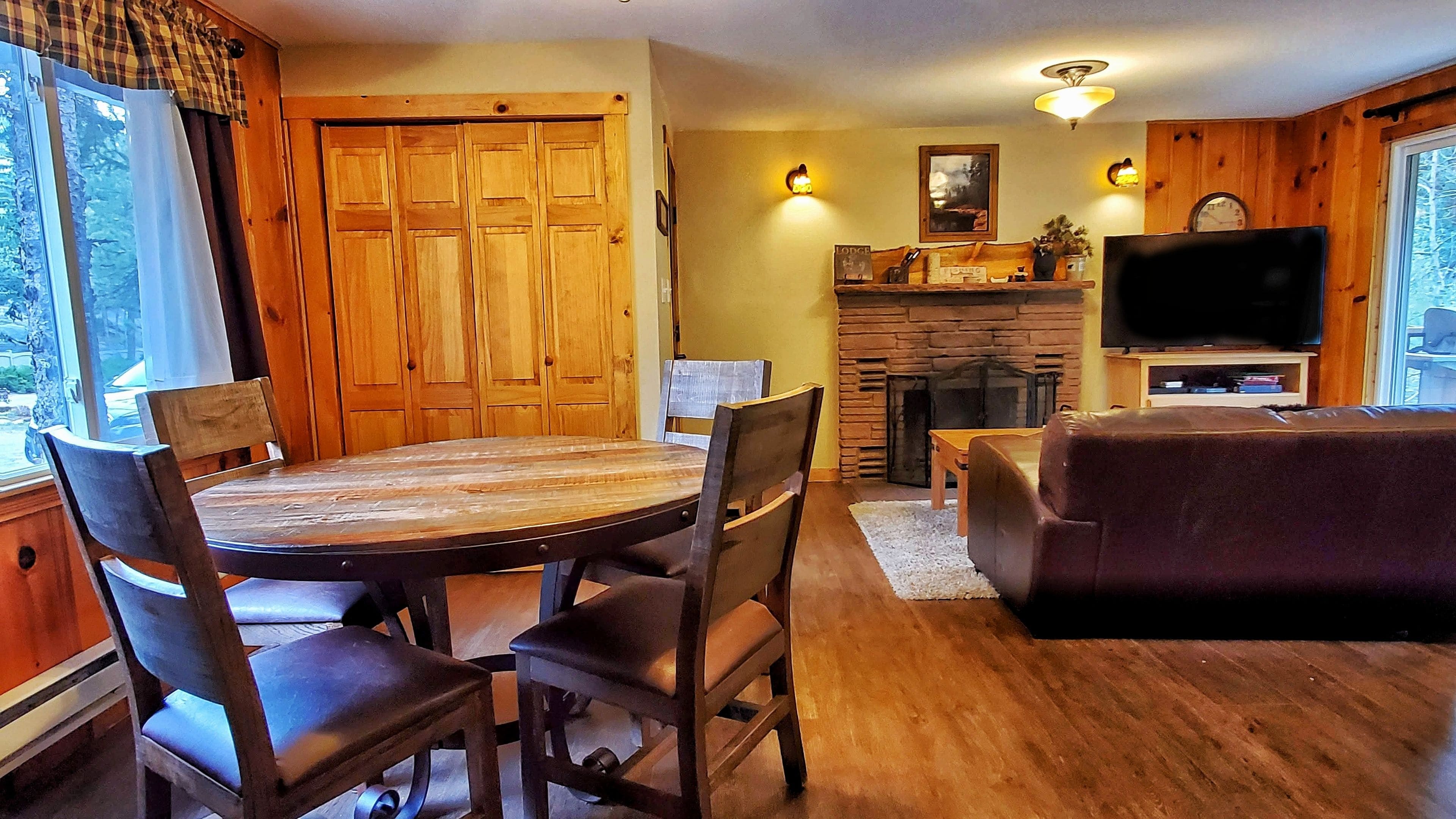A wooden interior with a dining table, chairs, a sofa, a fireplace, and a television.