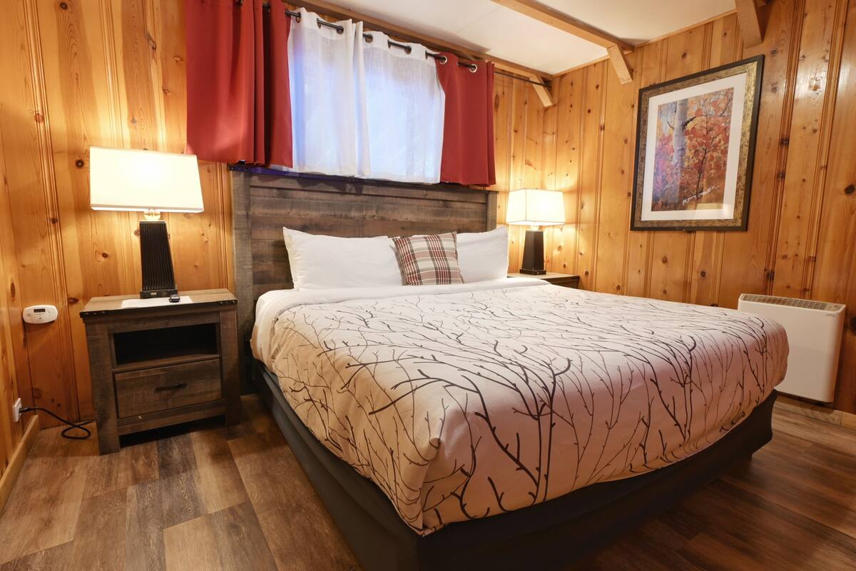 Une chambre à coucher aux murs lambrissés, avec un lit, deux lampes de chevet, une table de chevet et un tableau encadré au mur.