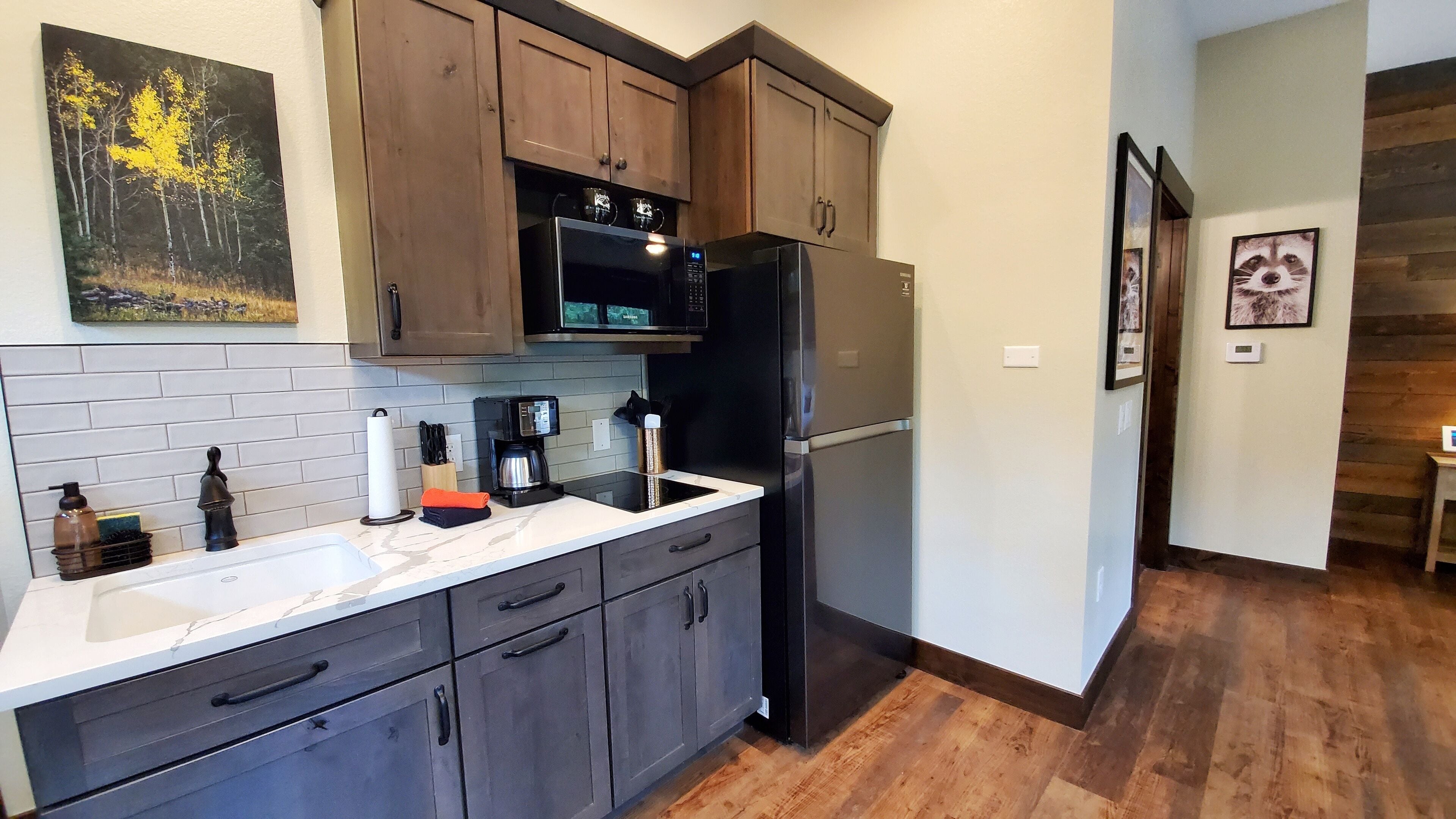 A modern kitchen with dark wooden cabinets, a stainless steel refrigerator, a microwave, and a coffee maker on the counter.