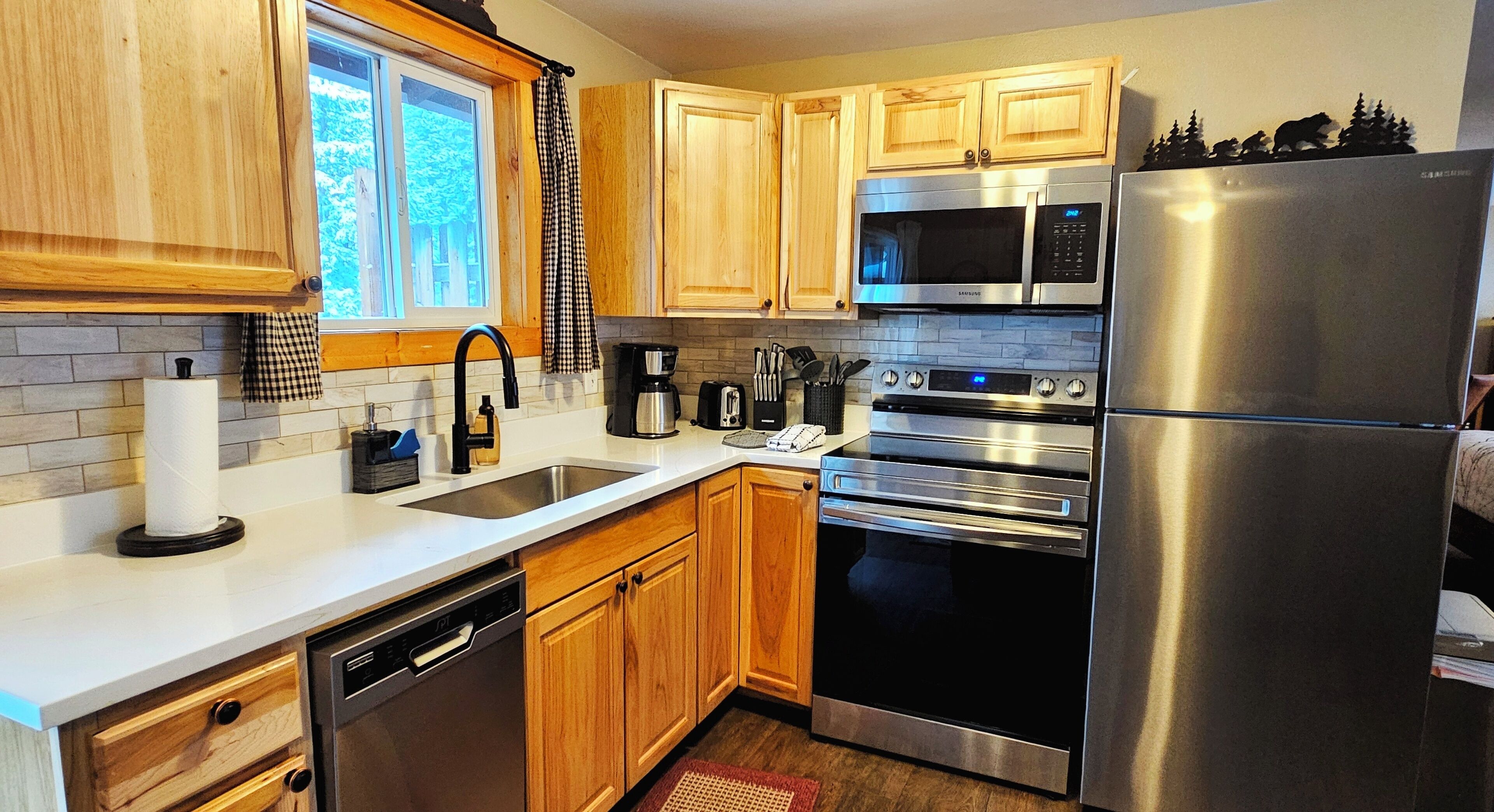 A modern kitchen with wooden cabinets, stainless steel appliances, and a window with a view of trees.