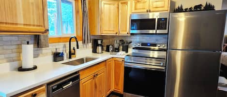 A modern kitchen with wooden cabinets, stainless steel appliances, and a window with a view of trees.