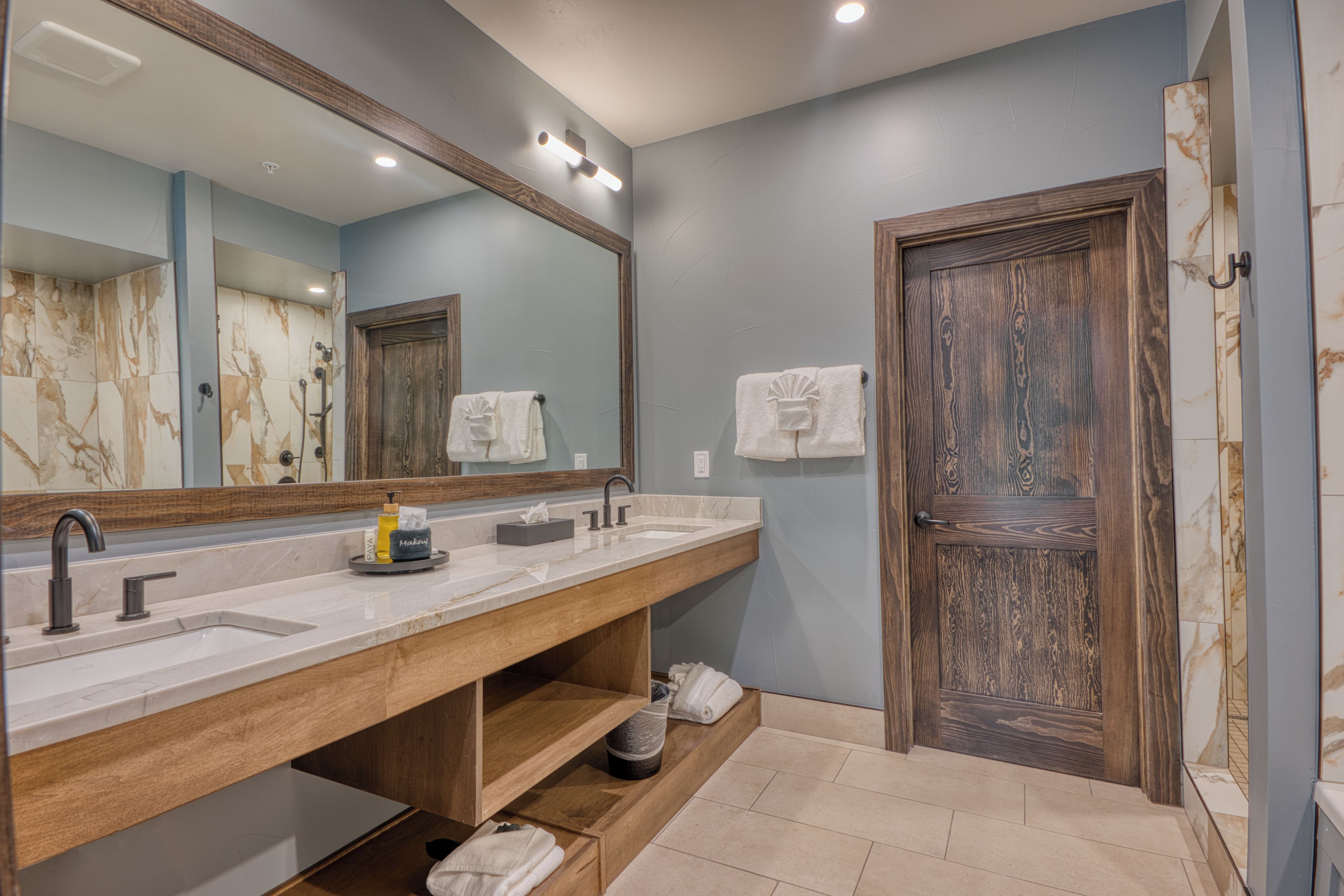 A bathroom with a wooden vanity, a large mirror, and a door with a textured design.