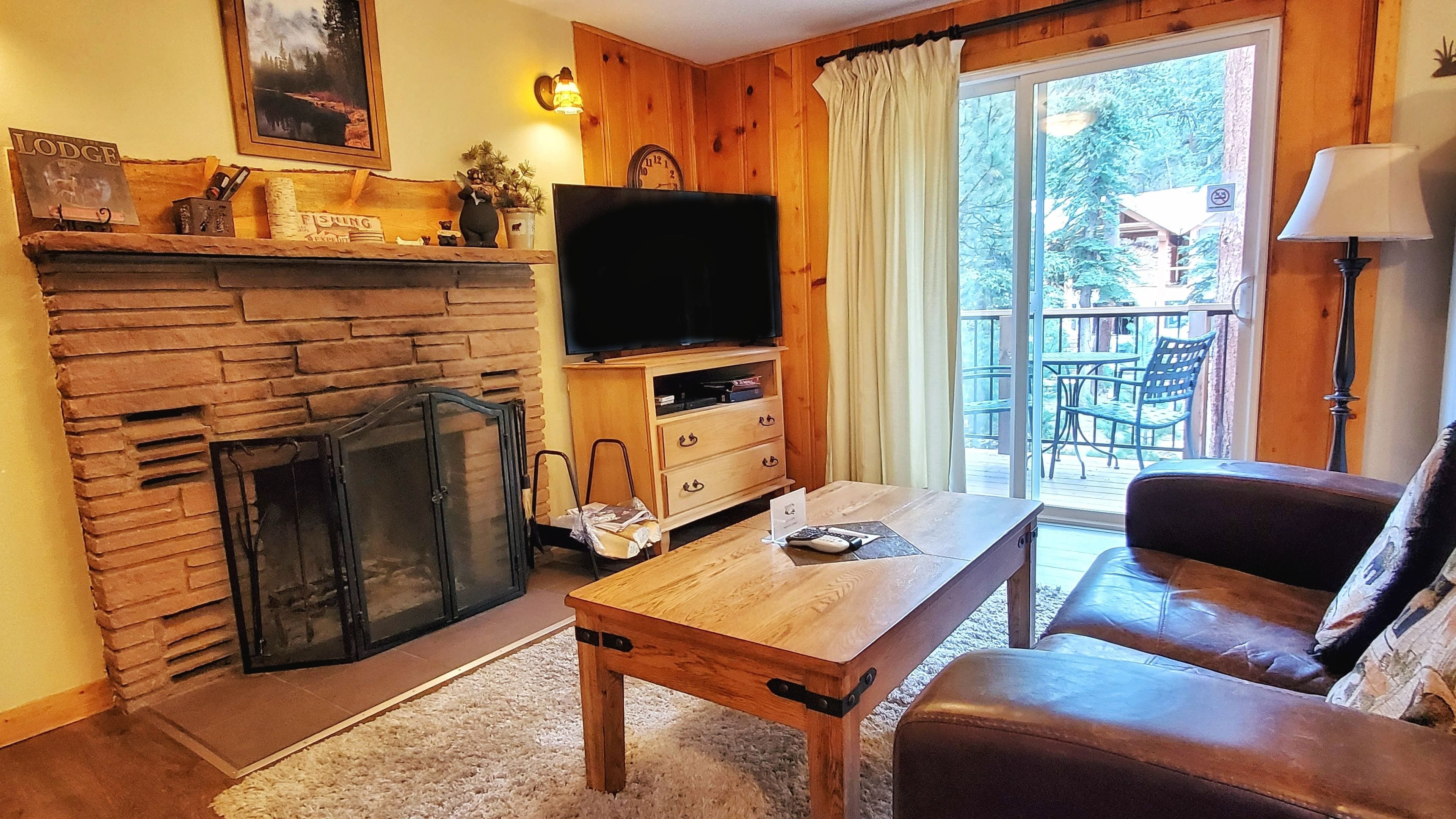 A cozy living room with a stone fireplace, a television, a wooden coffee table, and a leather sofa.