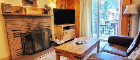 Ett mysigt vardagsrum med en steneldstad, en tv, ett träbord och en soffa klädd i läder.