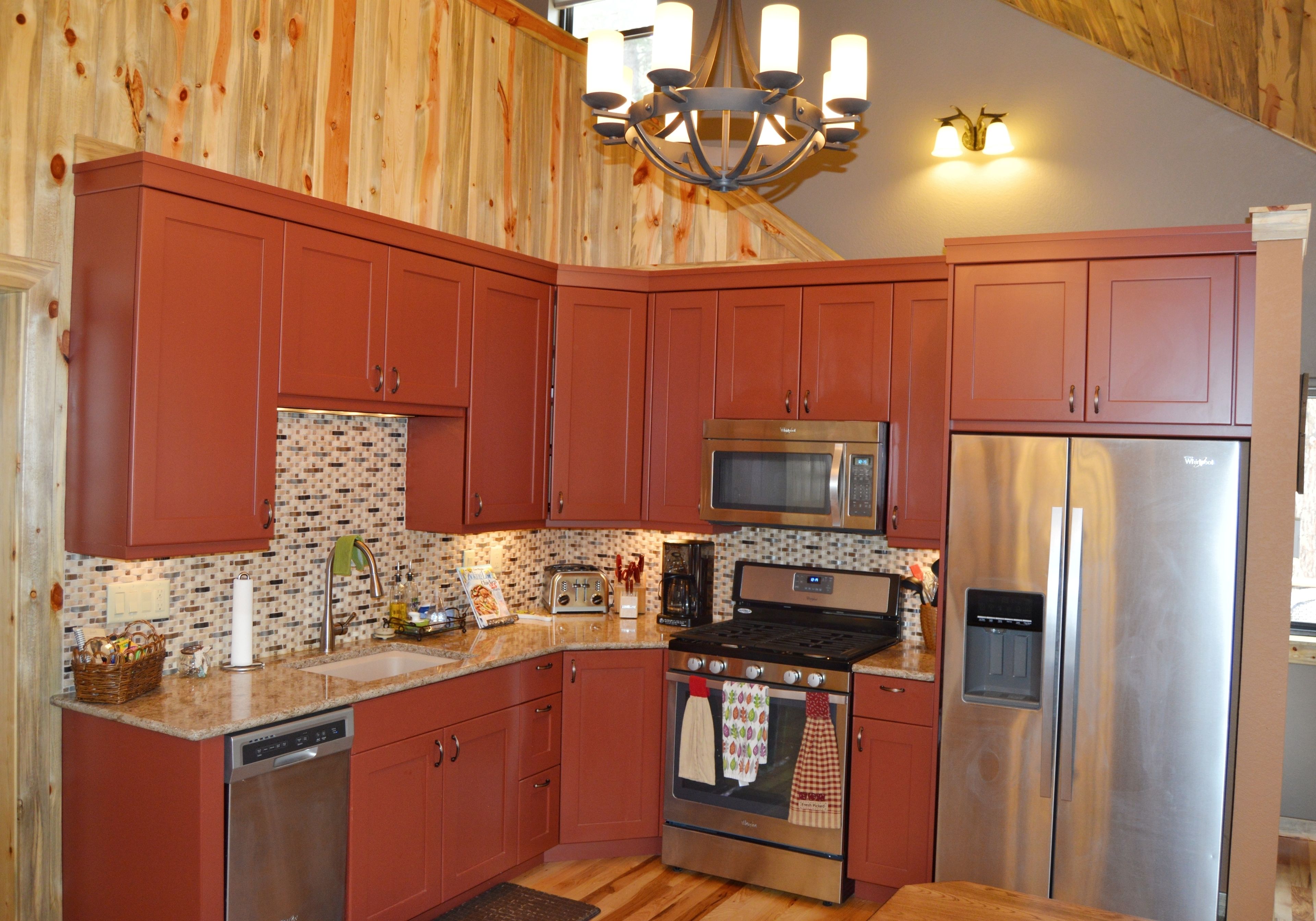 A kitchen with wooden paneling, a stainless steel refrigerator, a microwave, a stove, and a dishwasher.