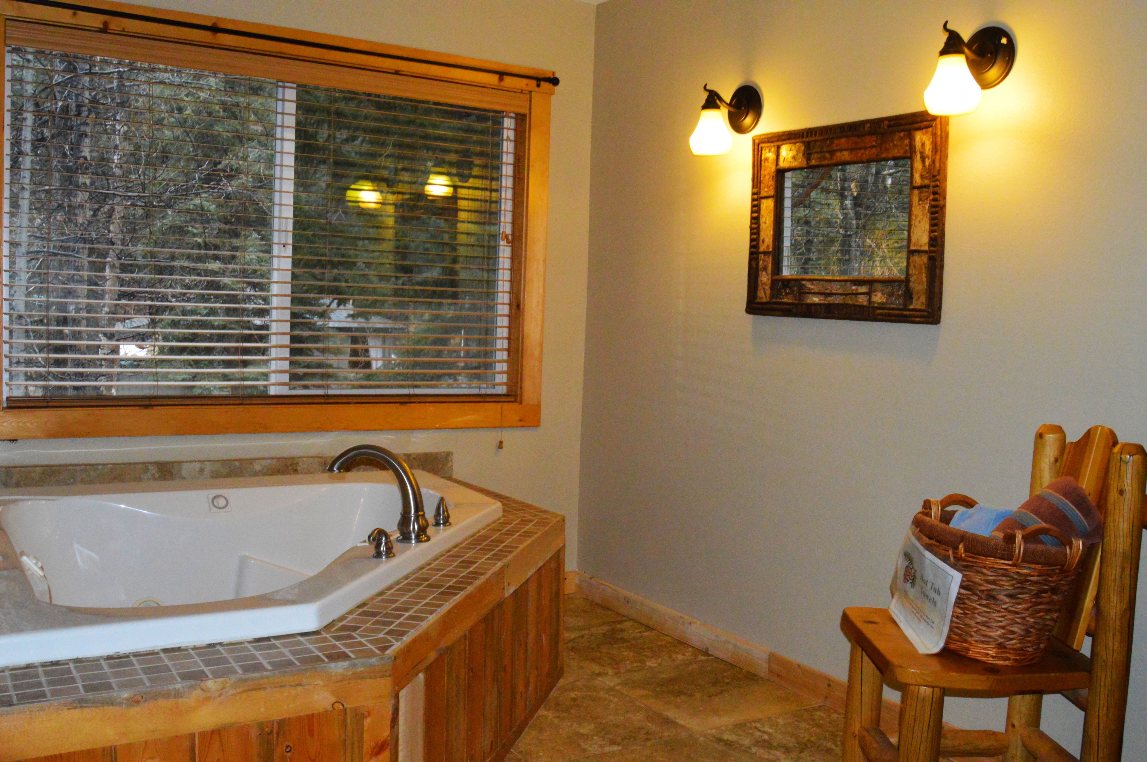 A bathroom with a large bathtub, wooden chair, and a wall-mounted light fixture.