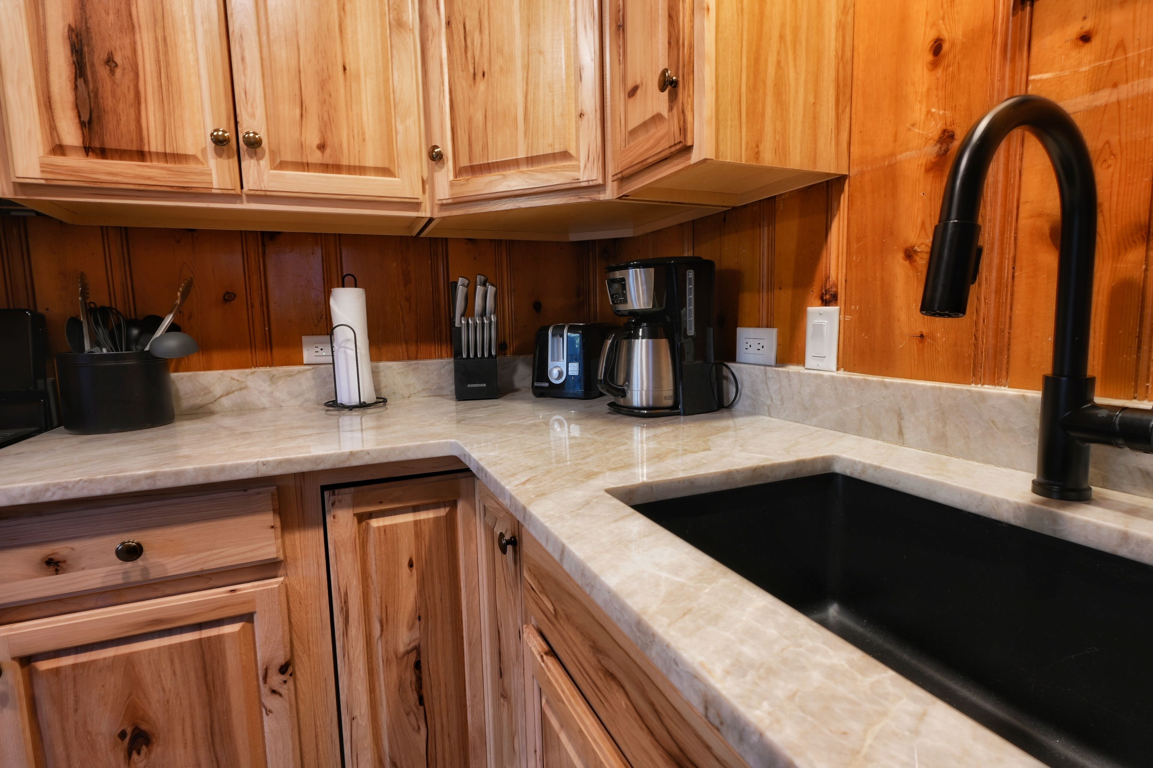 A kitchen with wooden cabinets, a black faucet, a coffee maker, and a toaster.